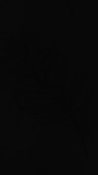 A shape sits in the upper half so dimly lit it is more suggestion than outline, the rest of the frame dropping to full black.