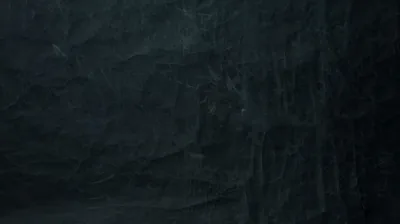 A near-black slate surface streaked with faint chalky smears, a cool blue-green cast lifting the upper left while the right half stays flat.