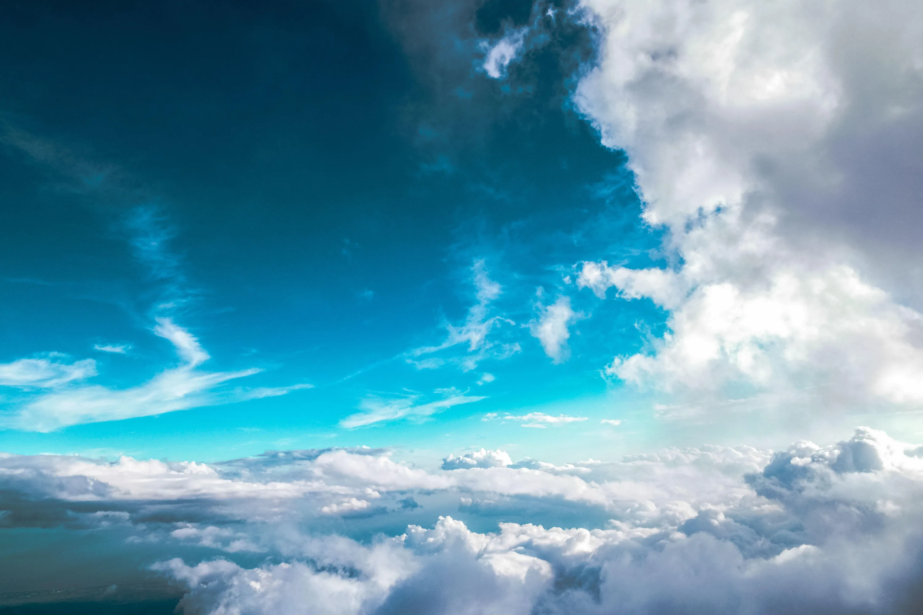 Looking out over a bright cloud deck from altitude, white cumulus stacked along the right while the left half stays open turquoise for icons.