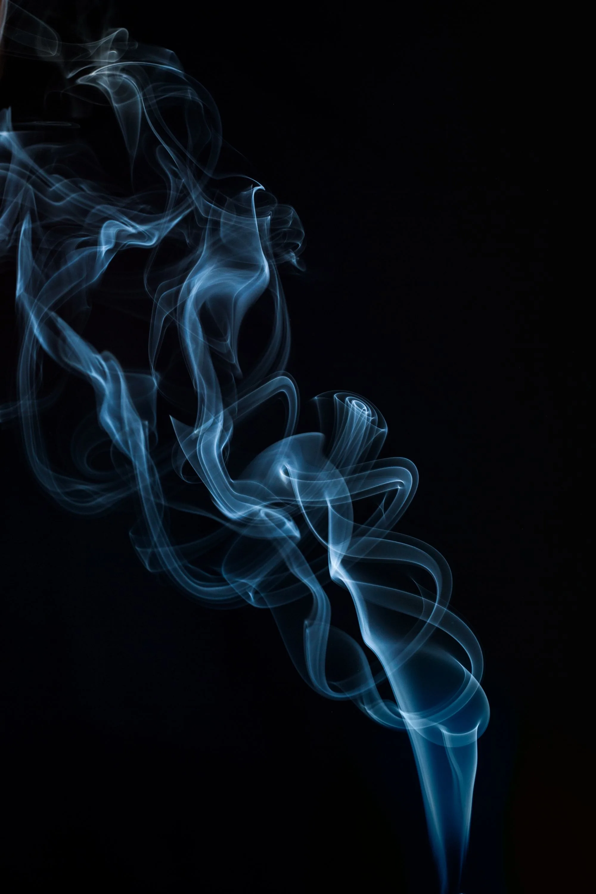 A single thread of pale blue smoke rises from the bottom edge and folds into loops, the right half of the frame kept empty.