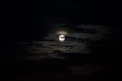 A full moon burns a small bright ring through thin night cloud, its faint warm halo fading fast so the corners stay fully black.