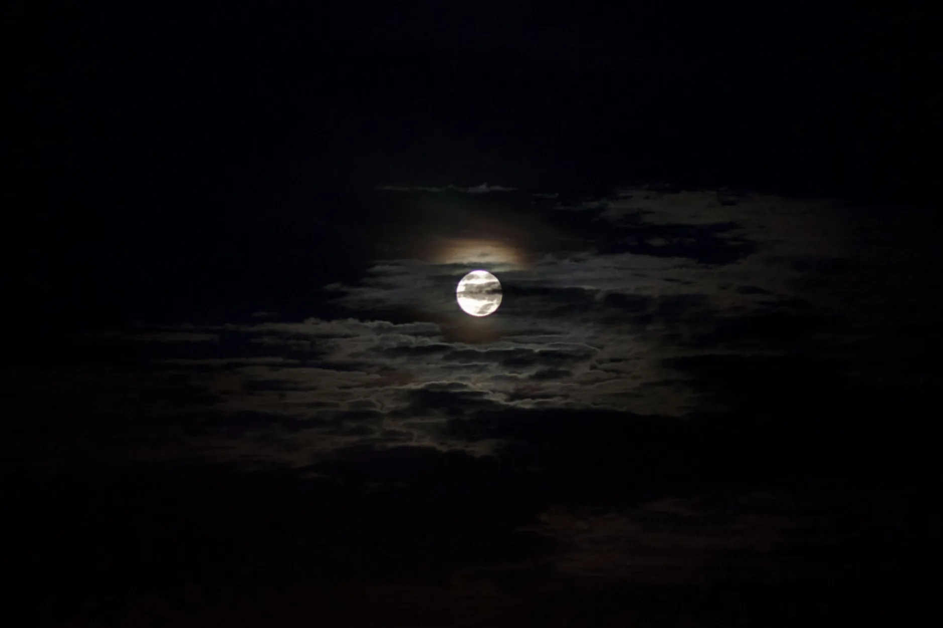 A full moon burns a small bright ring through thin night cloud, its faint warm halo fading fast so the corners stay fully black.