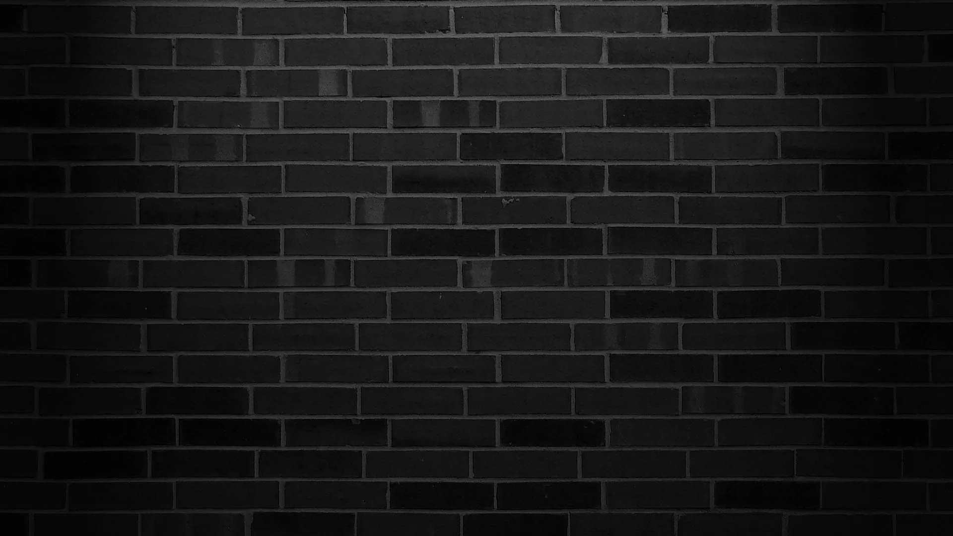 Smooth dark bricks laid in even courses, a wash of light across the upper half leaving the bottom edge in shadow.