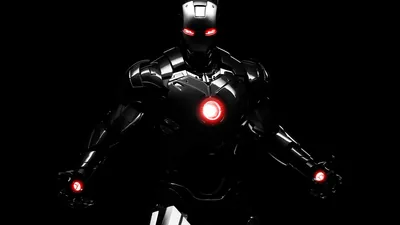 The armoured suit steps forward out of total black, red light burning at the chest, eyes and palms while the rest of the frame stays empty.