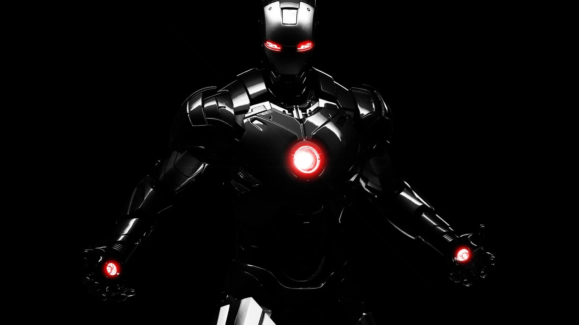 The armoured suit steps forward out of total black, red light burning at the chest, eyes and palms while the rest of the frame stays empty.