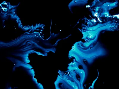 Bright cyan ink curls and branches through black liquid, the densest marbling gathering along the bottom and right of the frame.