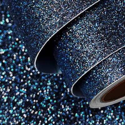 Rolled sheets of peel-and-stick glitter material catch the light, dense navy sparkle broken up by scattered teal and silver flecks, sharpest in the lower left.