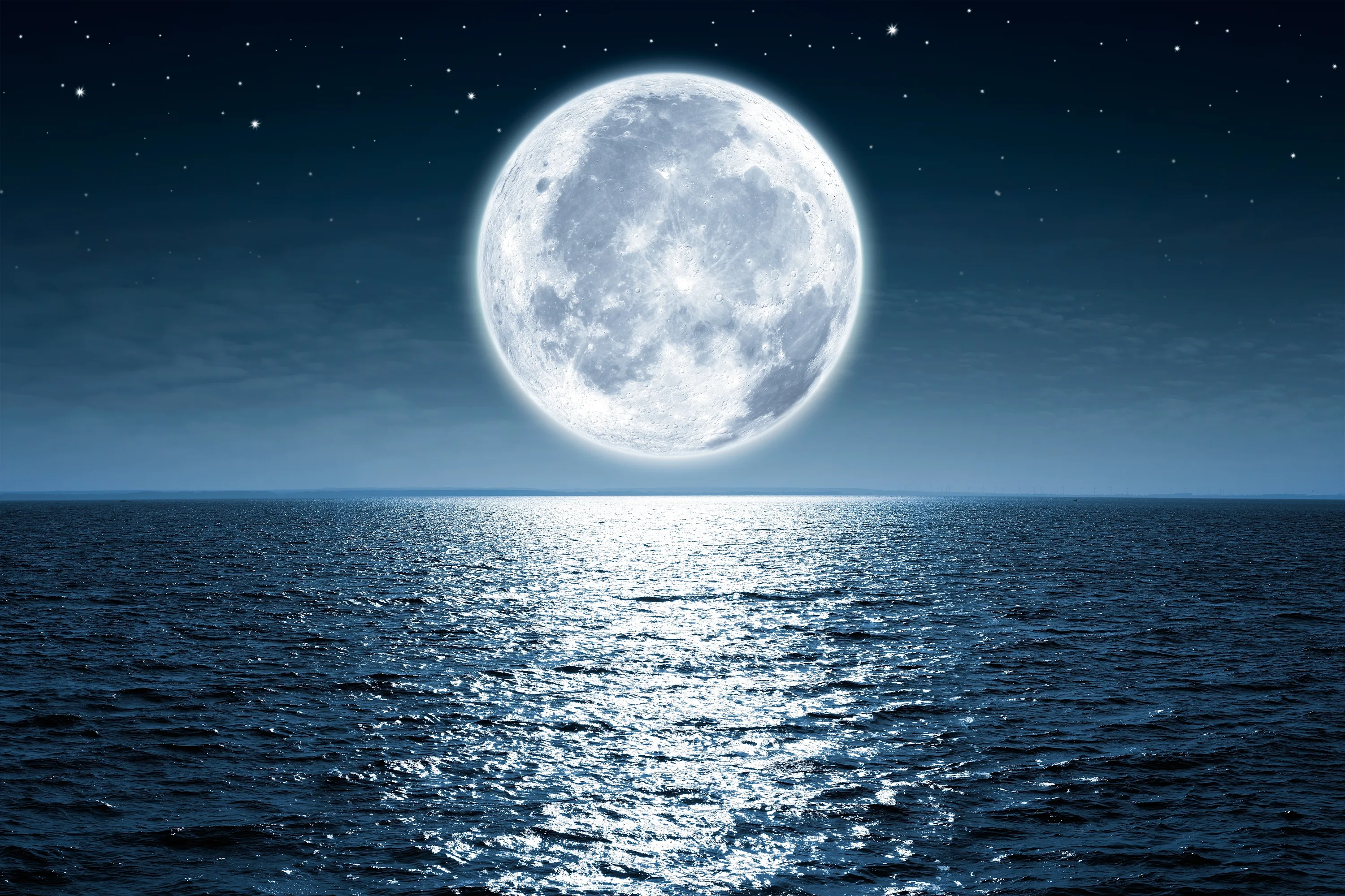 A full moon lays a sparkling path of light down the open sea, the horizon set low so sky fills most of the frame.