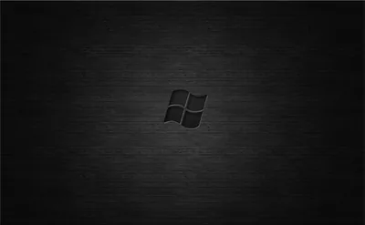 The four-pane mark sits centred on a brushed dark surface, the light pooling behind it and the corners left in shadow.