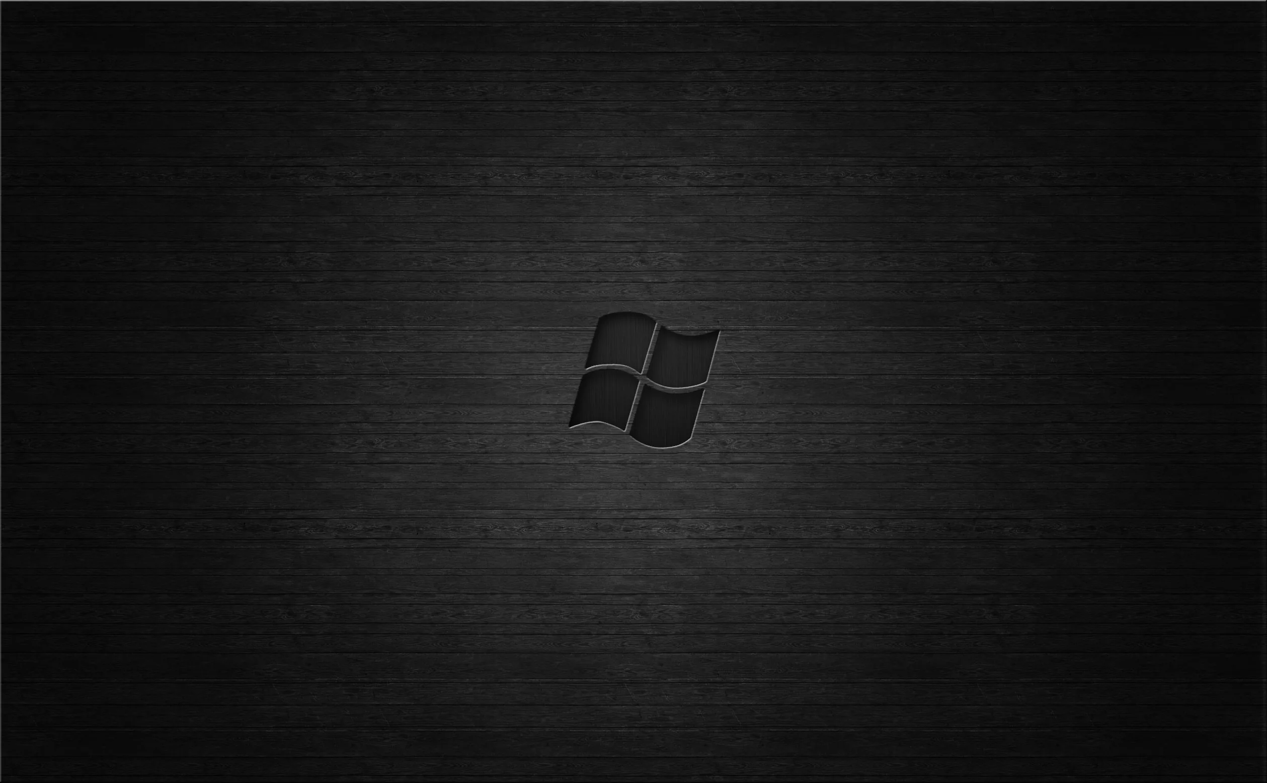 The four-pane mark sits centred on a brushed dark surface, the light pooling behind it and the corners left in shadow.