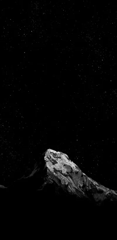 A bare rock summit catches moonlight at the bottom of the frame while stars scatter thinly across the black above it.