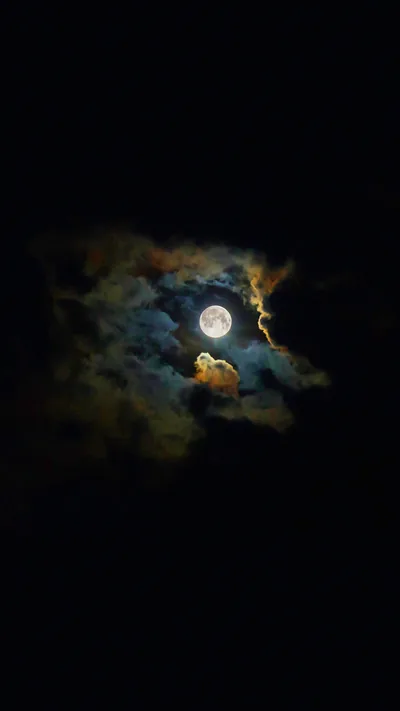 The moon burns through a break in thin cloud, warm light bleeding into the vapour and the rest of the sky left black.
