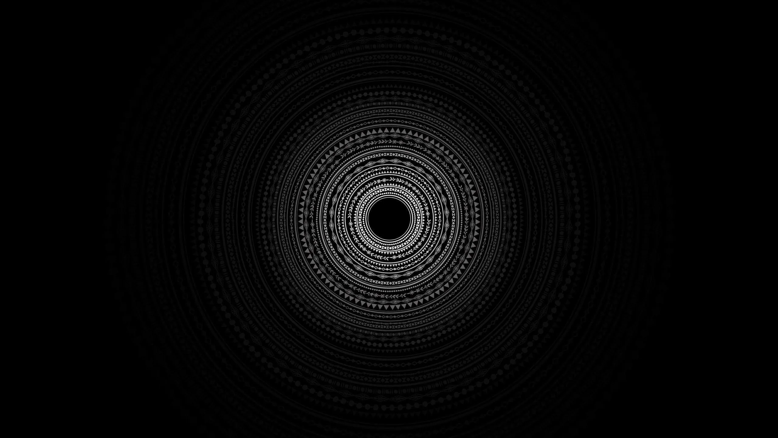 Concentric rings of fine white line work build a mandala at the centre, everything outside it left black.