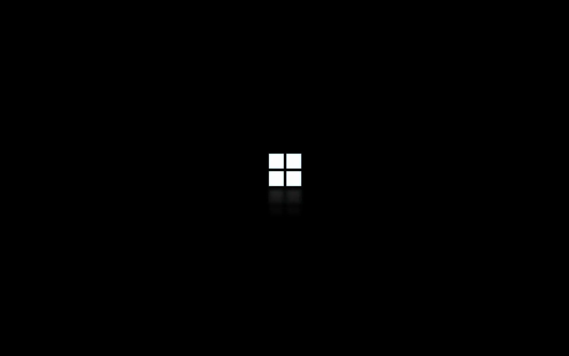 The four-pane Windows mark glows small and white at the centre of a true black frame, with a faint reflection below it.