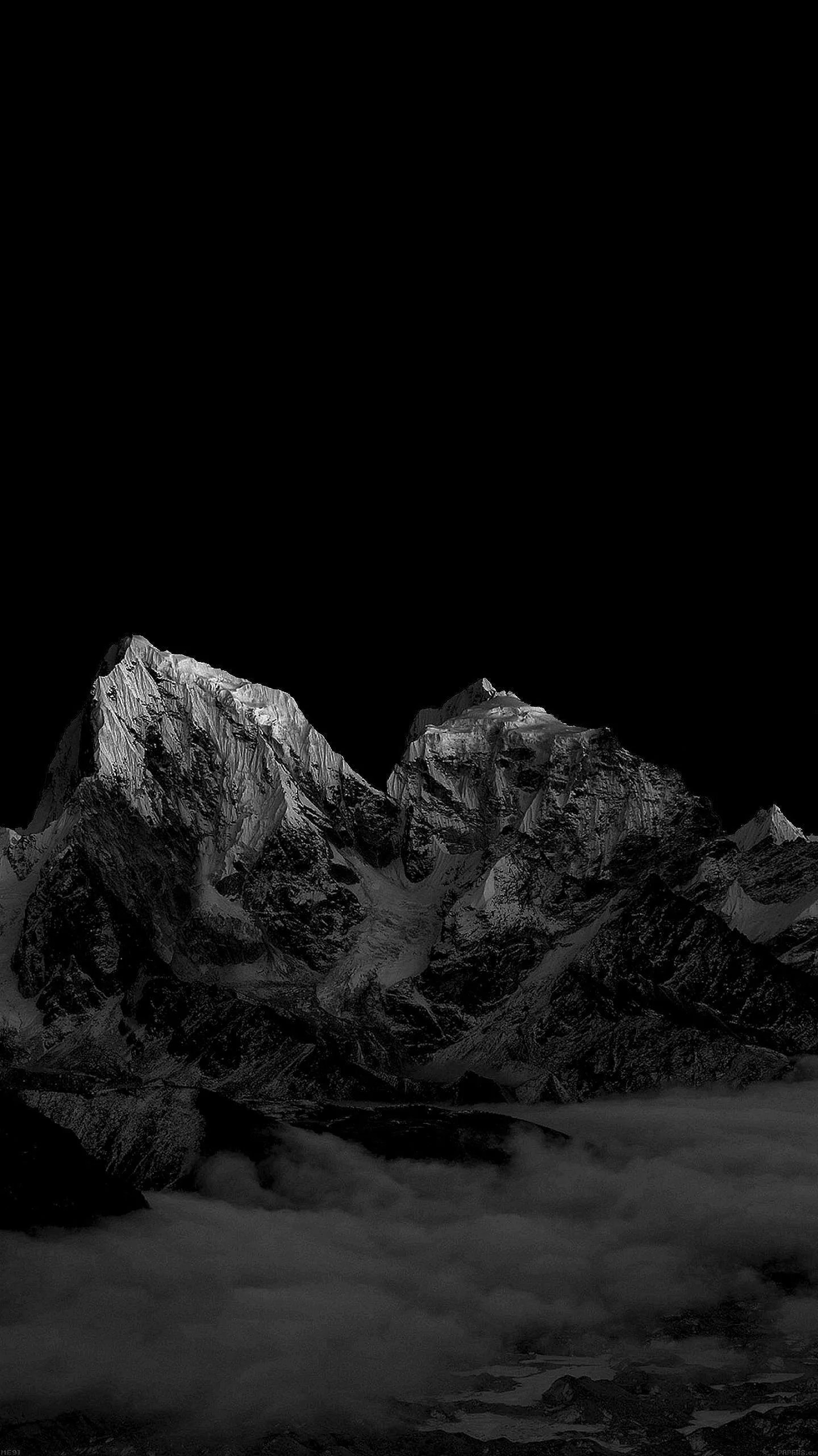 Two monochrome summits rise out of a cloud bank in the lower half of a tall frame, the sky above them left completely dark.