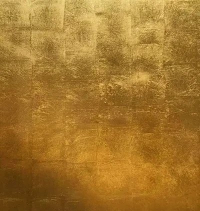 A gilded wall of overlapping gold leaf squares, each tile catching the light differently as the surface deepens to amber near the base.