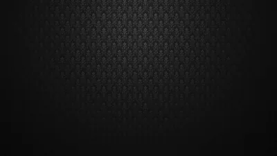 A tight fleur-de-lis print embossed on near-black fabric, centre lit and the outer frame dropping into shadow.