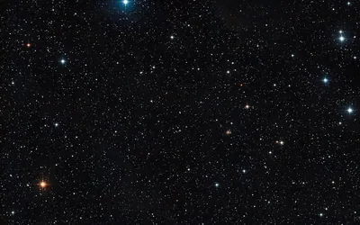 A dense scatter of stars in white, blue and amber across black space, one orange point standing out at the lower left.