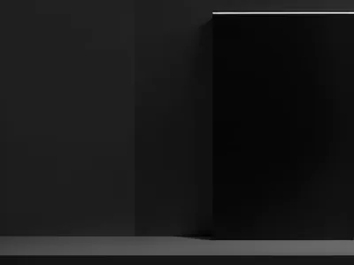 A glossy black panel stands against a matte grey wall with a thin strip of light along its top edge, casting a soft shadow onto the shelf below.