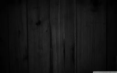 Vertical wood boards in charcoal, the grain and knots visible where a dim light grazes across from the left.