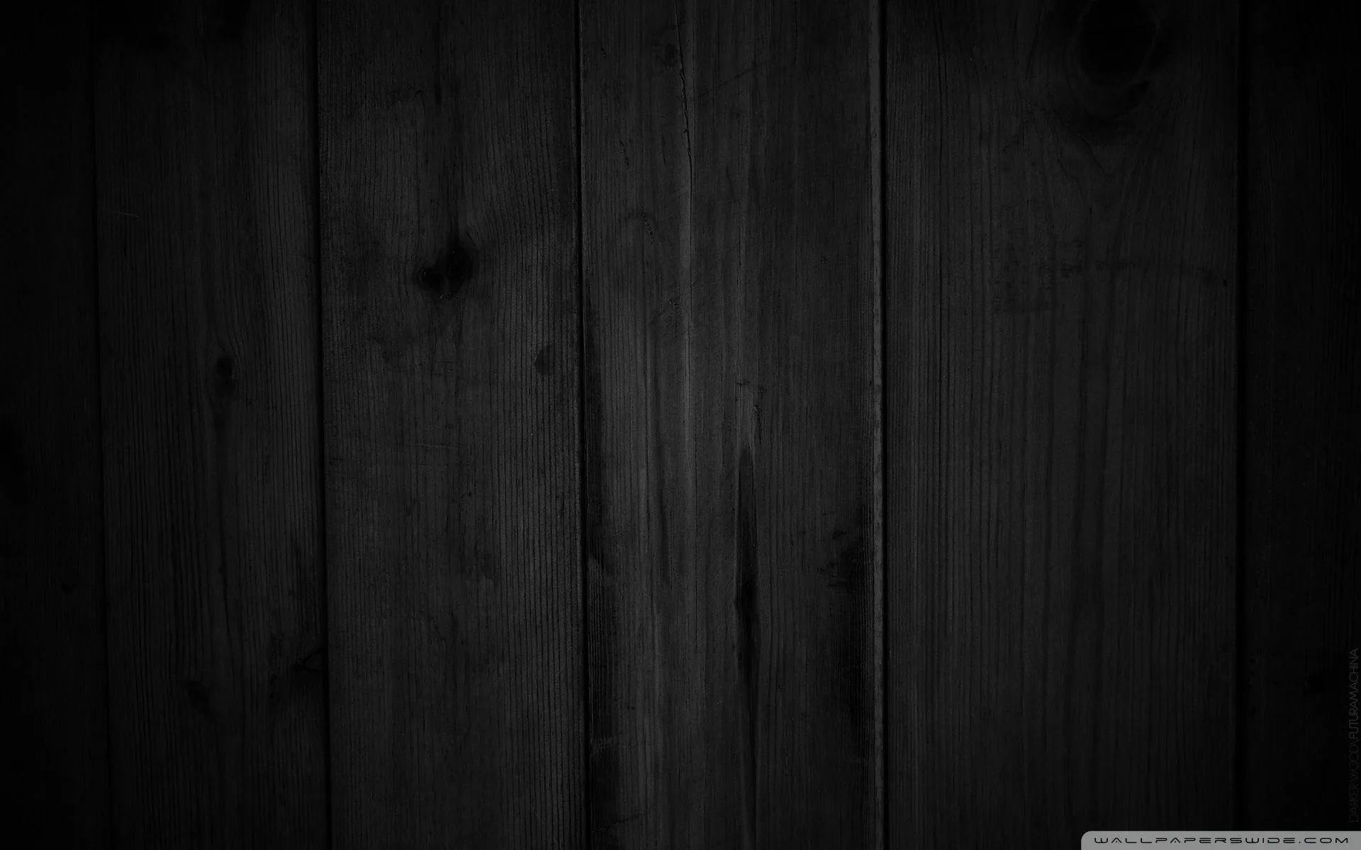 Vertical wood boards in charcoal, the grain and knots visible where a dim light grazes across from the left.