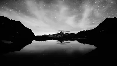 Stars and thin cloud sit above a peak that reflects whole in still water, the ridges on both sides reduced to flat black silhouettes.