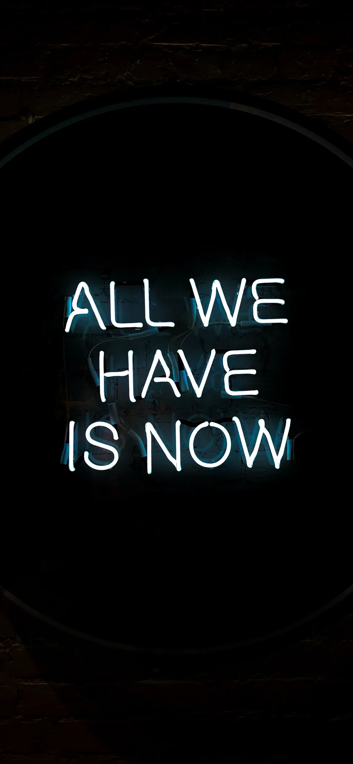 Pale blue neon letters spell out the phrase inside a dark circular frame, the wall around it barely visible.