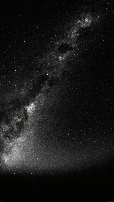 The same diagonal star band shot in monochrome, dark rifts running through its brightest section and a low haze lifting off the horizon.