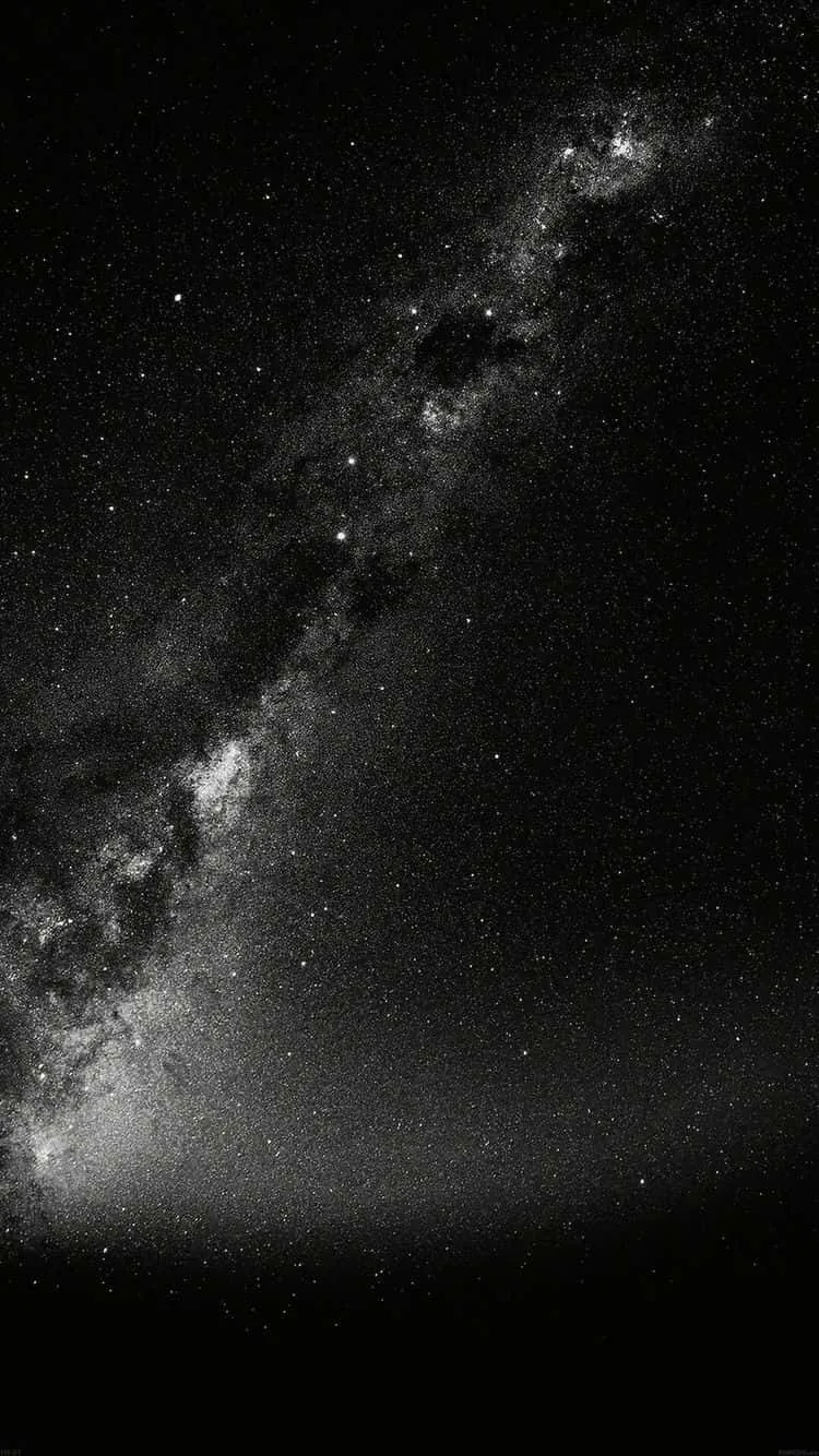 The same diagonal star band shot in monochrome, dark rifts running through its brightest section and a low haze lifting off the horizon.