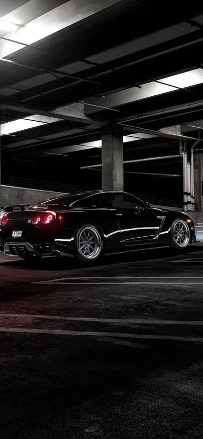 Vertical shot of a black Mustang on the empty top deck of a car park, red tail lamps lit and strip lighting running away along the ceiling.