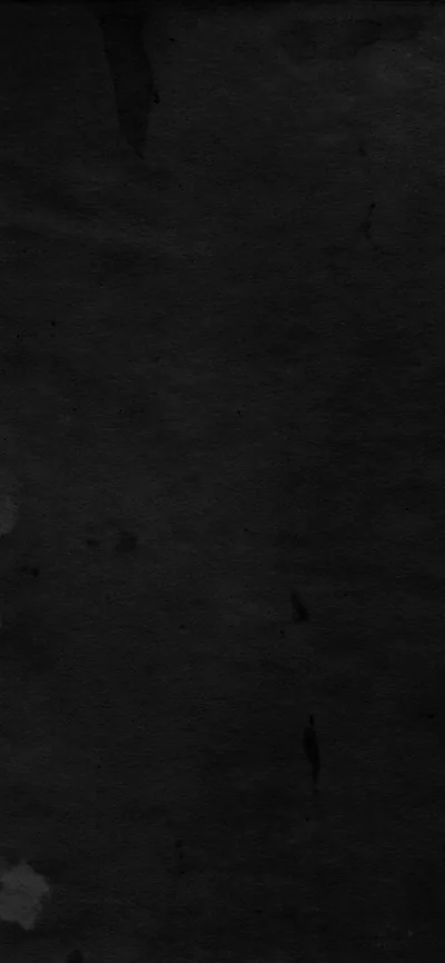 A flat black wall with faint scuffs and paint marks, the surface grain visible only where a little light falls across the upper left.