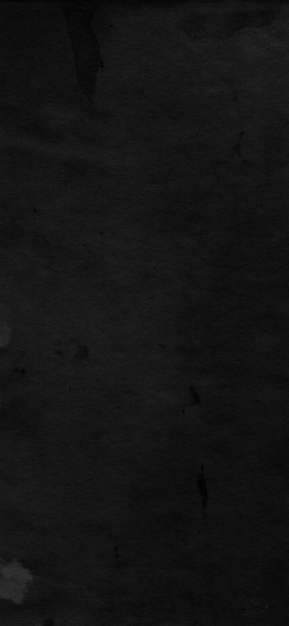 A flat black wall with faint scuffs and paint marks, the surface grain visible only where a little light falls across the upper left.