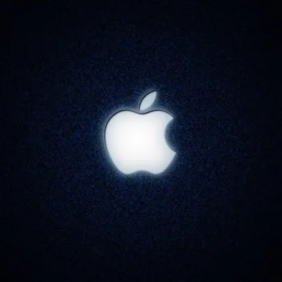 A white Apple mark glows at the centre of a coarse dark denim square, the fabric grain fading into shadow at every corner.