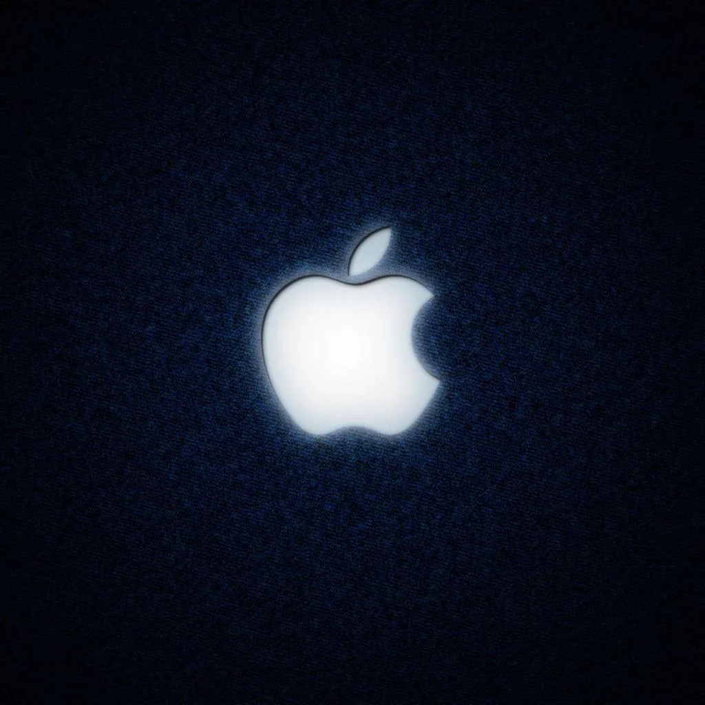 A white Apple mark glows at the centre of a coarse dark denim square, the fabric grain fading into shadow at every corner.