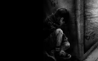 Monochrome shot of a boy hugging his knees at the base of a scratched wall; the entire left half is solid black, ready for icons or widgets.