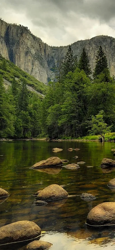 Boulders step up the river toward grey granite walls, a thin waterfall visible top left under an overcast sky that mutes every colour to green and stone.