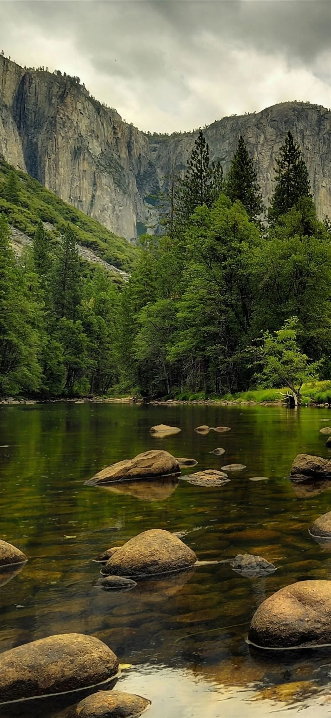Boulders step up the river toward grey granite walls, a thin waterfall visible top left under an overcast sky that mutes every colour to green and stone.