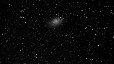 A small faint spiral floats above centre in a grainy monochrome star field, small enough that most of the frame is just stars.