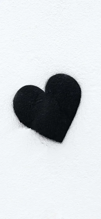 A single black heart cut from rough felt sits slightly off-centre on a white textured sheet, its edges fuzzy where the fibres catch.