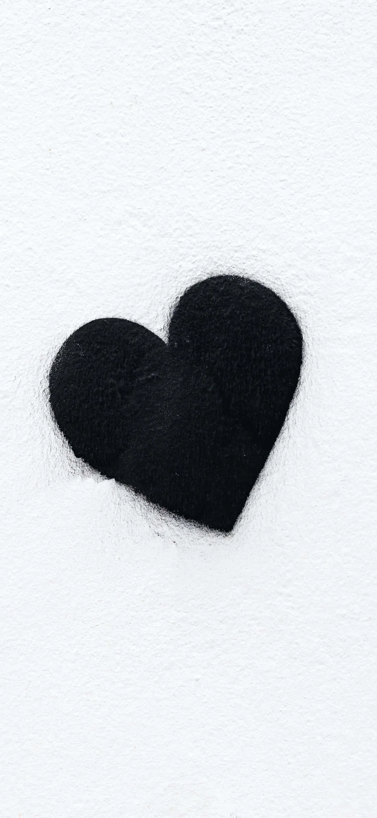 A single black heart cut from rough felt sits slightly off-centre on a white textured sheet, its edges fuzzy where the fibres catch.