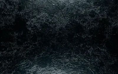 Craggy hammered black metal fills the frame, light from above skimming the ridges while a wet-looking sheen gathers along the bottom edge.
