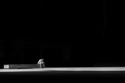 Darkness fills the top three quarters of the frame; only a narrow band of daylight along the bottom catches a man slumped beside a low ledge.