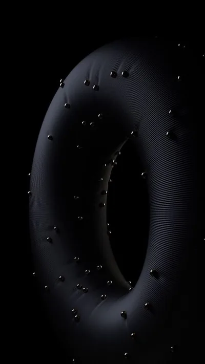 A ribbed black ring floats against pure black with beads of water clinging across its surface, each drop catching a small hard highlight.