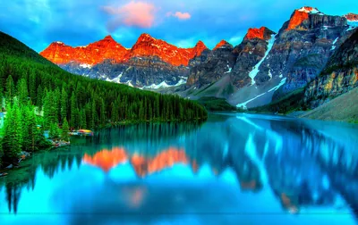 Alpenglow paints the row of ten peaks orange above a blue glacial lake, every summit repeated in the water; the widescreen spread loses its symmetry in a phone crop.