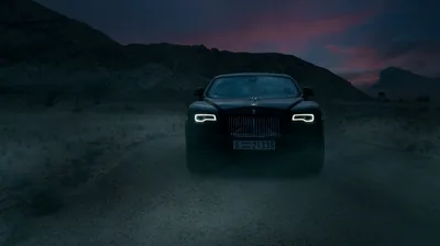 The coupe faces the camera on a dirt track, grille and daytime running lamps glowing faintly against a purple and pink dusk over dry hills.