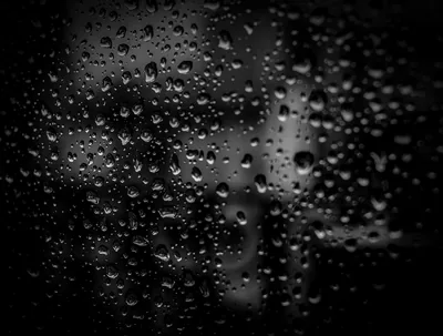 Water beads cling to a pane of glass, city light behind them dissolved into soft grey blur and deep black.