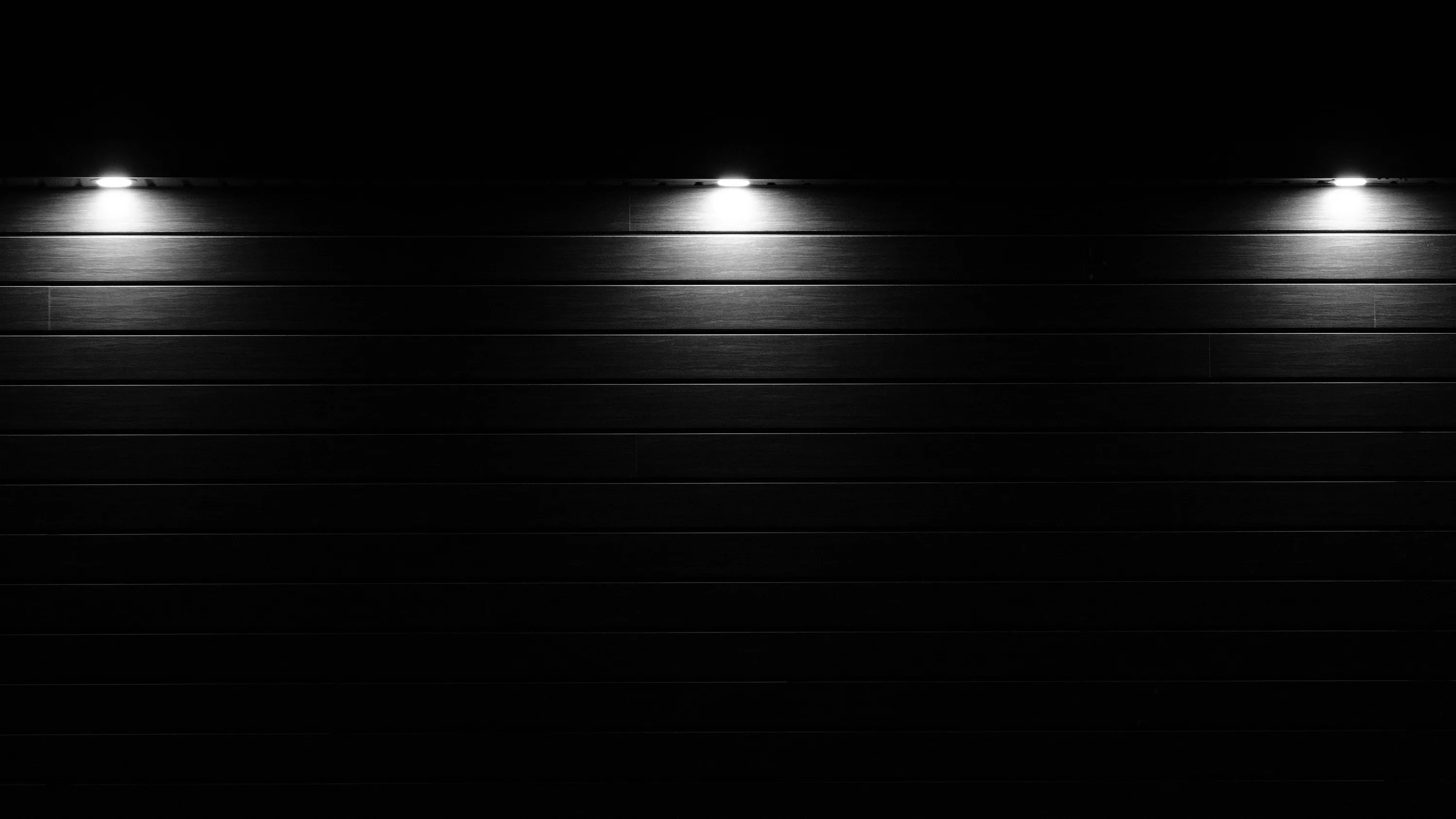 Three lamps throw overlapping cones of light down a panelled concrete wall, the corners left in full black.