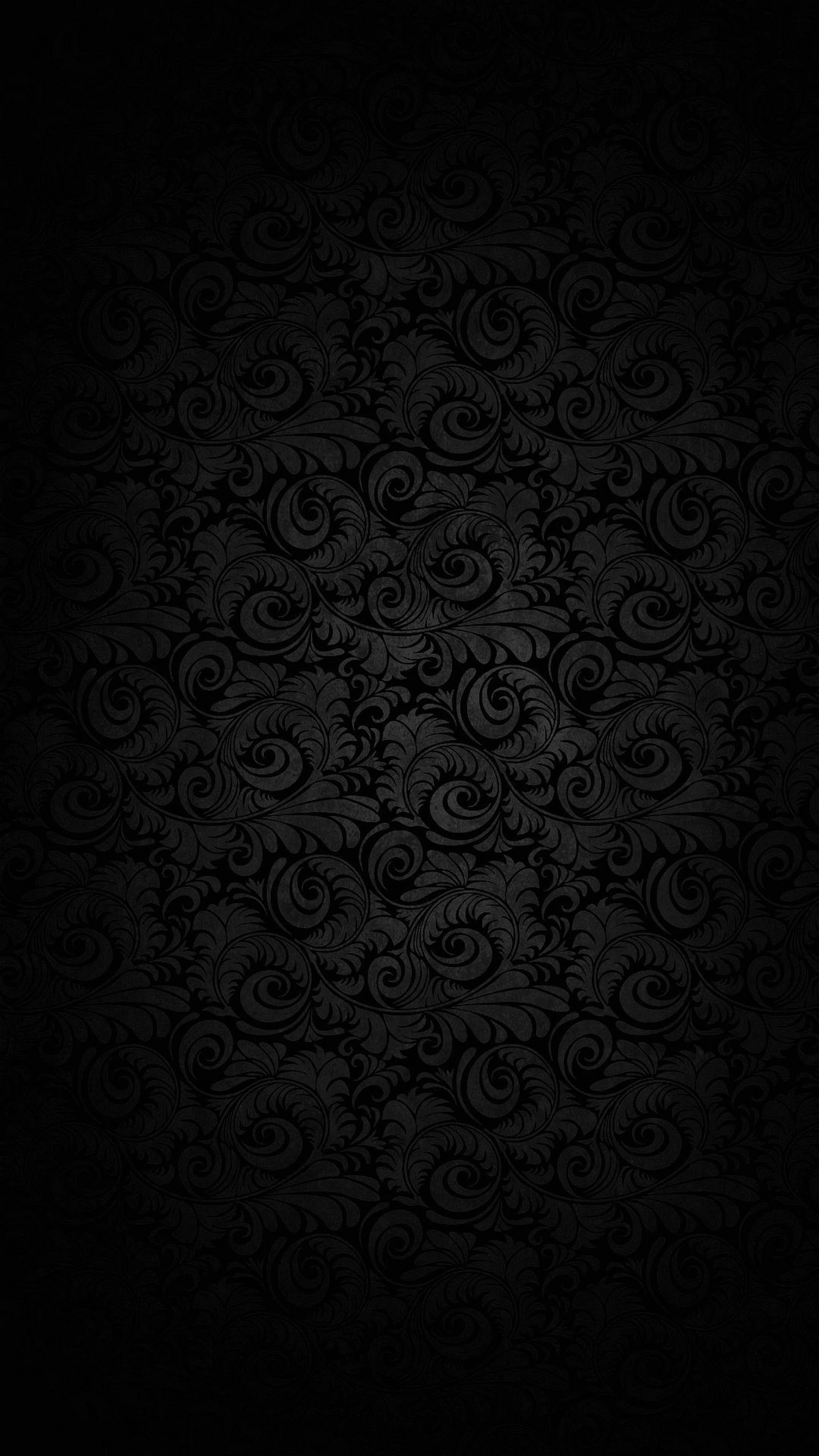 A repeating damask print on dark wallpaper, lit faintly in the middle so the edges and all four corners fall away into black.