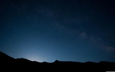 A faint Milky Way band crosses the upper right of a deep blue night, hills reduced to a black strip along the bottom for OLED screens.