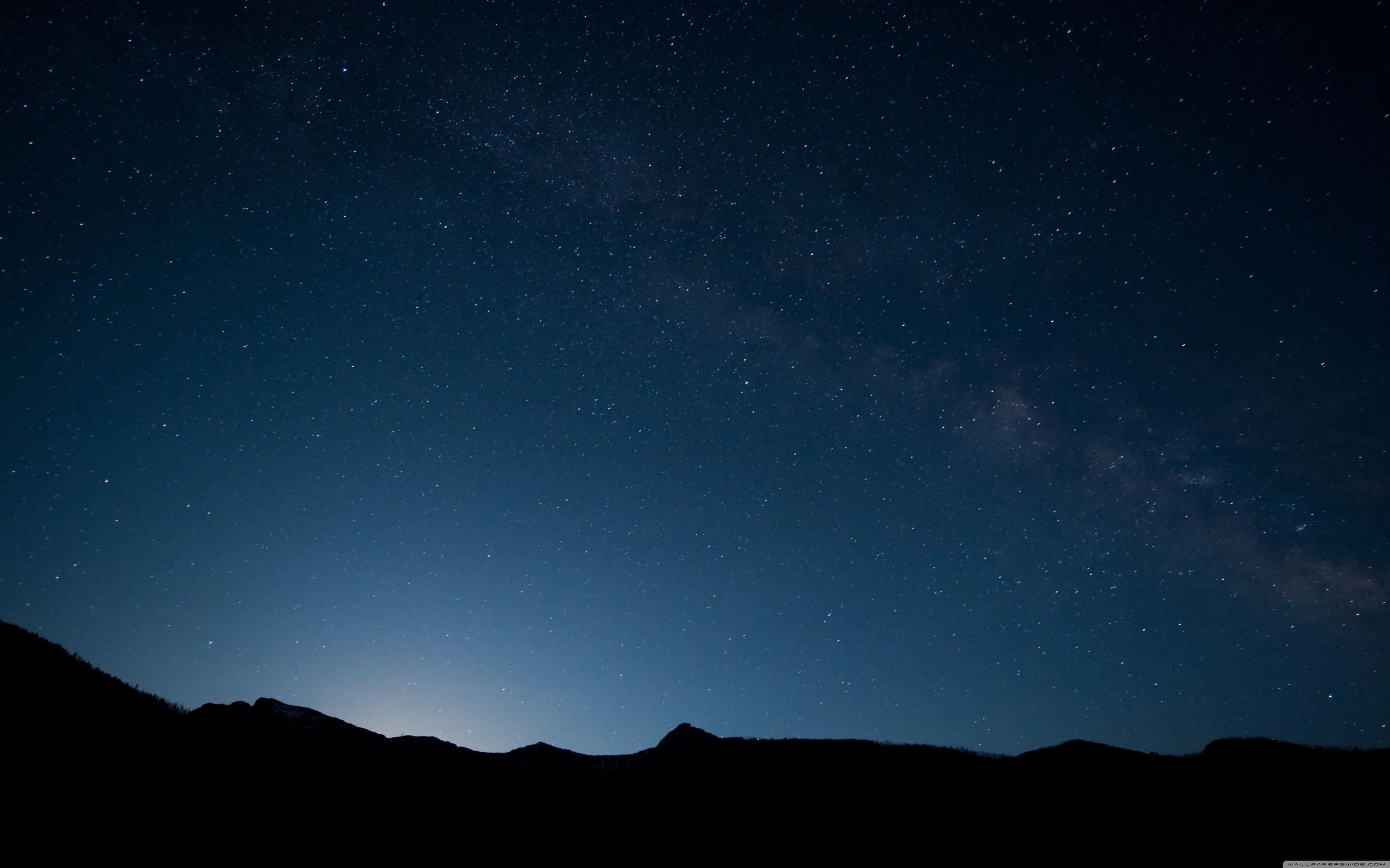 A faint Milky Way band crosses the upper right of a deep blue night, hills reduced to a black strip along the bottom for OLED screens.